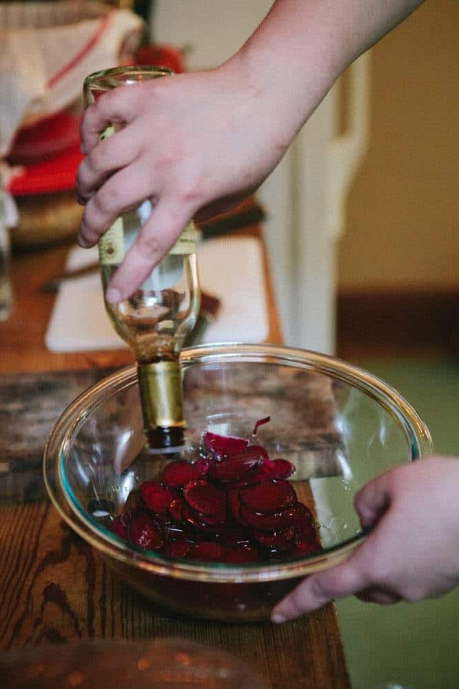 Person pouring vinegar into a bowl of beets